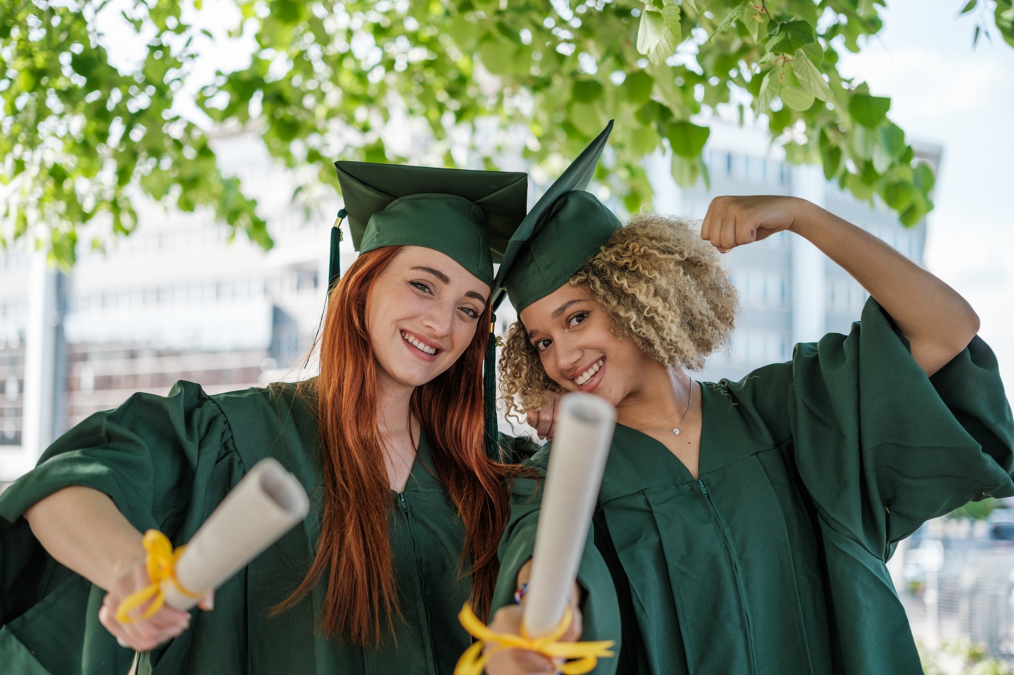 Two young women with university degrees in their hands on their graduation day: studies, education